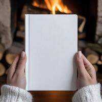 Cozy hands hold a blank notebook near a warm fireplace photo