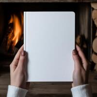 Hands holding a blank notebook by a cozy fireplace photo