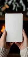 Hands holding a blank notebook in front of a cozy fireplace photo