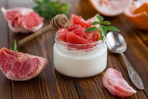 homemade sweet yogurt in a glass jar with pieces of red ripe grapefruit and honey, on a wooden table photo