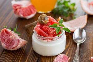 homemade sweet yogurt in a glass jar with pieces of red ripe grapefruit and honey, on a wooden table photo