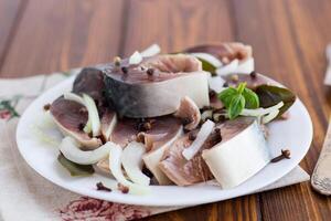 lightly salted mackerel with onions and spices, in a plate on a wooden table photo
