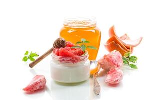 homemade sweet yogurt in a glass jar with pieces of red ripe grapefruit and honey, isolated on white background photo