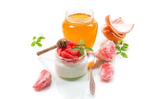 homemade sweet yogurt in a glass jar with pieces of red ripe grapefruit and honey, isolated on white background photo