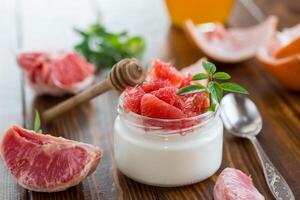 homemade sweet yogurt in a glass jar with pieces of red ripe grapefruit and honey, on a wooden table . photo