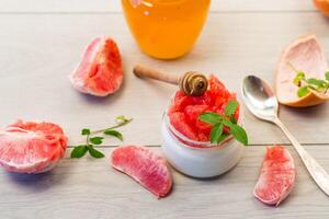 homemade sweet yogurt in a glass jar with pieces of red ripe grapefruit and honey, on a wooden table photo
