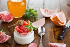 homemade sweet yogurt in a glass jar with pieces of red ripe grapefruit and honey, on a wooden table photo