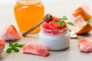 homemade sweet yogurt in a glass jar with pieces of red ripe grapefruit and honey, on a wooden table photo