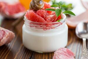 homemade sweet yogurt in a glass jar with pieces of red ripe grapefruit and honey, on a wooden table photo