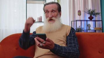 Senior grandfather at home use smartphone typing browsing, wow yes found out great big win celebrate video