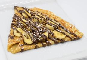 Pancakes with banana and chocolate on a white plate photo