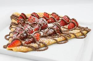 Crepe with strawberries and chocolate on a white plate. photo