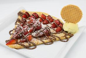 Crepe with strawberries and chocolate on a white plate. photo