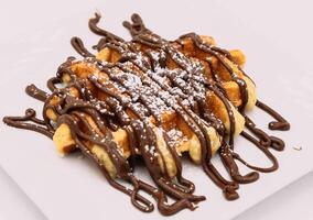 Belgian waffles with chocolate syrup on a white plate closeup photo