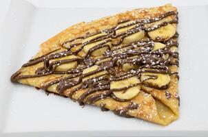 Pancakes with banana and chocolate on a white plate photo