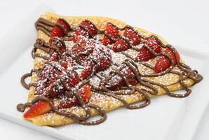 Crepe with strawberries and chocolate on a white plate. photo