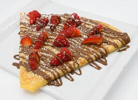Crepe with strawberries and chocolate on a white plate. photo