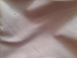 a close-up view of a light-colored fabric with visible folds and subtle shadows, showcasing its texture and softness. photo