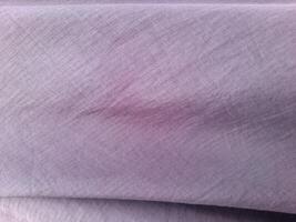 A close-up view of a light purple fabric with a fine, diagonal line pattern. The surface appears soft and smooth, with subtle folds that create a gentle texture, ideal for garments or home decor. photo