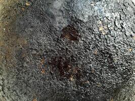a heavily burned and blackened surface, a scorched pan or cooking utensil, with a textured and cracked appearance due to carbonized residue. photo