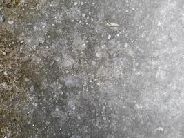 a close-up view of a weathered concrete surface. The concrete is predominantly gray in color, with a rough and uneven texture. photo