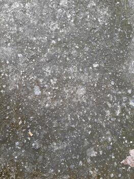 a close-up view of a weathered concrete surface. The concrete is predominantly gray in color, with a rough and uneven texture. photo