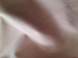 a close-up view of a light-colored fabric with visible folds and subtle shadows, showcasing its texture and softness. photo