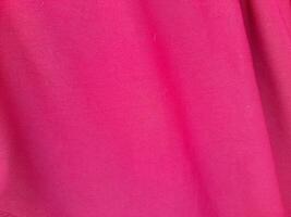 A close-up view of vibrant pink fabric with a smooth and slightly textured surface. The image showcases a diagonal fold, highlighting the fabric's soft drape and rich color. photo