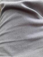 a close-up of a piece of gray fabric. The fabric appears to be woven, with a subtle texture visible in the weave. The color is a uniform, medium gray, with no discernible pattern or design. photo