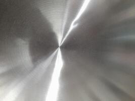 a close-up image of a brushed stainless steel surface. The circular brushing pattern is clearly visible, creating a textured appearance with fine lines radiating from the center. photo