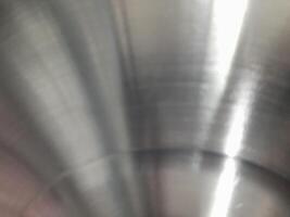 a close-up image of a brushed stainless steel surface. The circular brushing pattern is clearly visible, creating a textured appearance with fine lines radiating from the center. photo