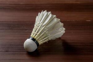 An isolated shuttlecock placed on a wooden table, showcasing its delicate feathers and intricate design. The simplicity of the scene highlights the shuttlecock details photo