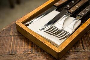 A wooden holder with cutlery, including a knife, fork, and napkin, arranged neatly. This setup gives a rustic and elegant dining atmosphere, ideal for table settings photo