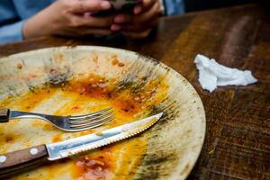 A cream-colored plate with a beautiful pattern shows leftover food, including a knife and fork. Some sauce remains on the plate, indicating the end of a meal photo
