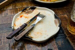 A cream-colored plate with a beautiful pattern shows leftover food, including a knife and fork. Some sauce remains on the plate, indicating the end of a meal photo