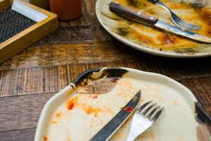 A cream-colored plate with a beautiful pattern shows leftover food, including a knife and fork. Some sauce remains on the plate, indicating the end of a meal photo