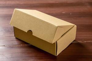 An isolated cardboard box placed on a wooden table, highlighting its simple design and natural texture. The photo emphasizes the box shape and the wooden surface beneath