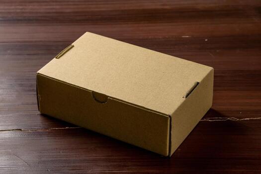 An isolated cardboard box placed on a wooden table, highlighting its simple design and natural texture. The photo emphasizes the box shape and the wooden surface beneath