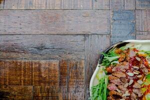 A flatlay shot of a beef salad topped with nuts and dressing, placed on a wooden table. The image also includes space for text, ideal for a customizable layout photo