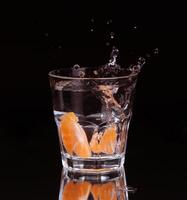 Slice of lemon splashing into a glass of water with a spray of water droplets in motion suspended in the air above the glass on a dark background. photo