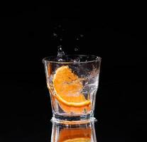 Slice of lemon splashing into a glass of water with a spray of water droplets in motion suspended in the air above the glass on a dark background. photo