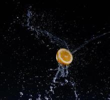 A high-speed shot of a lemon with splashing water, on a black background. photo