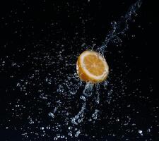 A high-speed shot of a lemon with splashing water, on a black background. photo