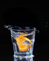 Slice of lemon splashing into a glass of water with a spray of water droplets in motion suspended in the air above the glass on a dark background. photo