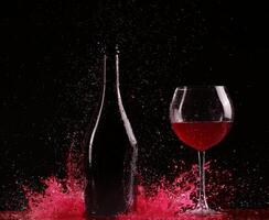 Glass and bottle of red wine splash on black photo