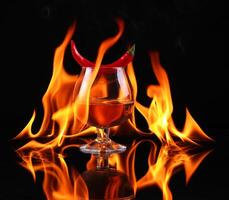 Hot chili pepper in a cognac ballon with a fire on a black background photo