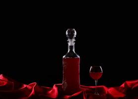glass and bottle of wine on a dark background silk photo