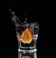 Slice of lemon splashing into a glass of water with a spray of water droplets in motion suspended in the air above the glass on a dark background. photo