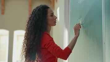 Smiling clever Hispanic student girl Latina woman Caucasian female lady teacher tutor studying learn writing chalk on blackboard formula math mathematic in class auditorium university college academy video