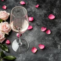 Elegant arrangement of wine glass with pink rose petals and fresh roses on dark surface photo